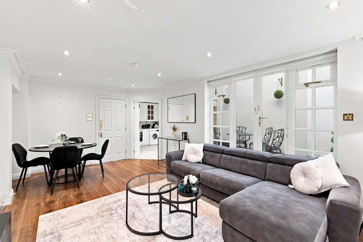 A modern living room with a grey sofa, a round coffee table, and a dining area with a white table and black chairs.