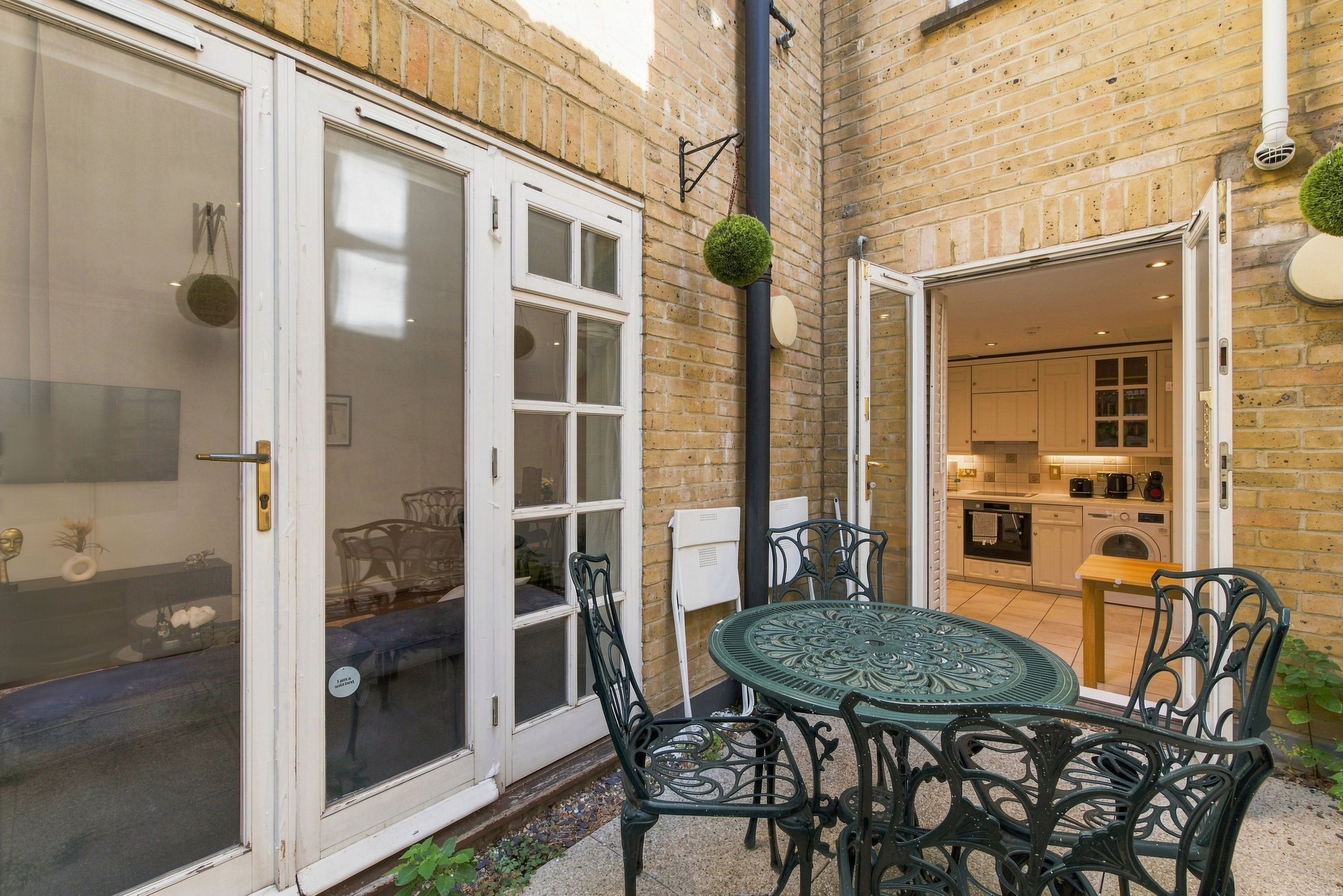 Un patio con una mesa y sillas, un muro de ladrillo y una puerta que da a una cocina.