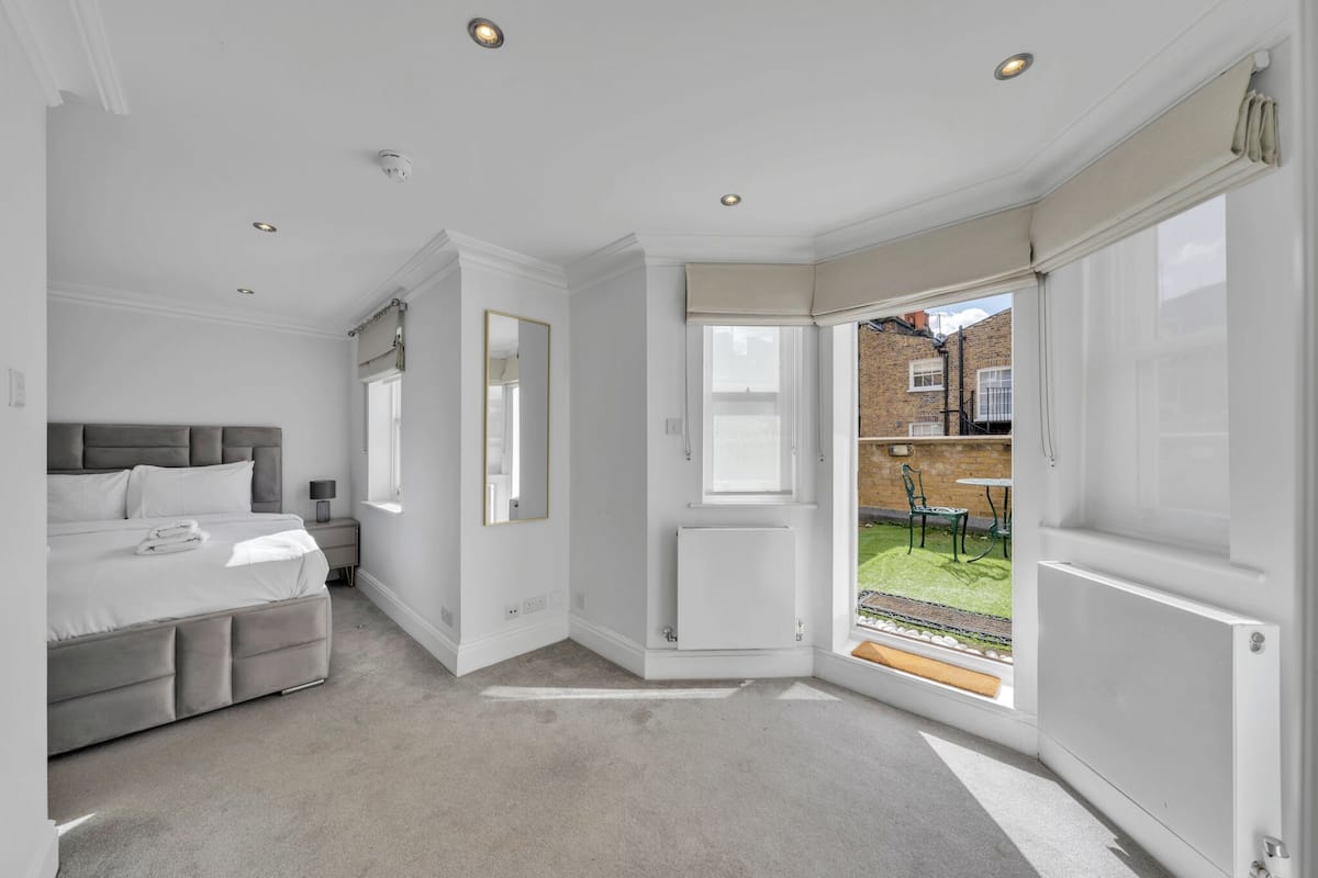 A bedroom with a large bed, a bedside table, a mirror, and a view of a garden through a sliding door.