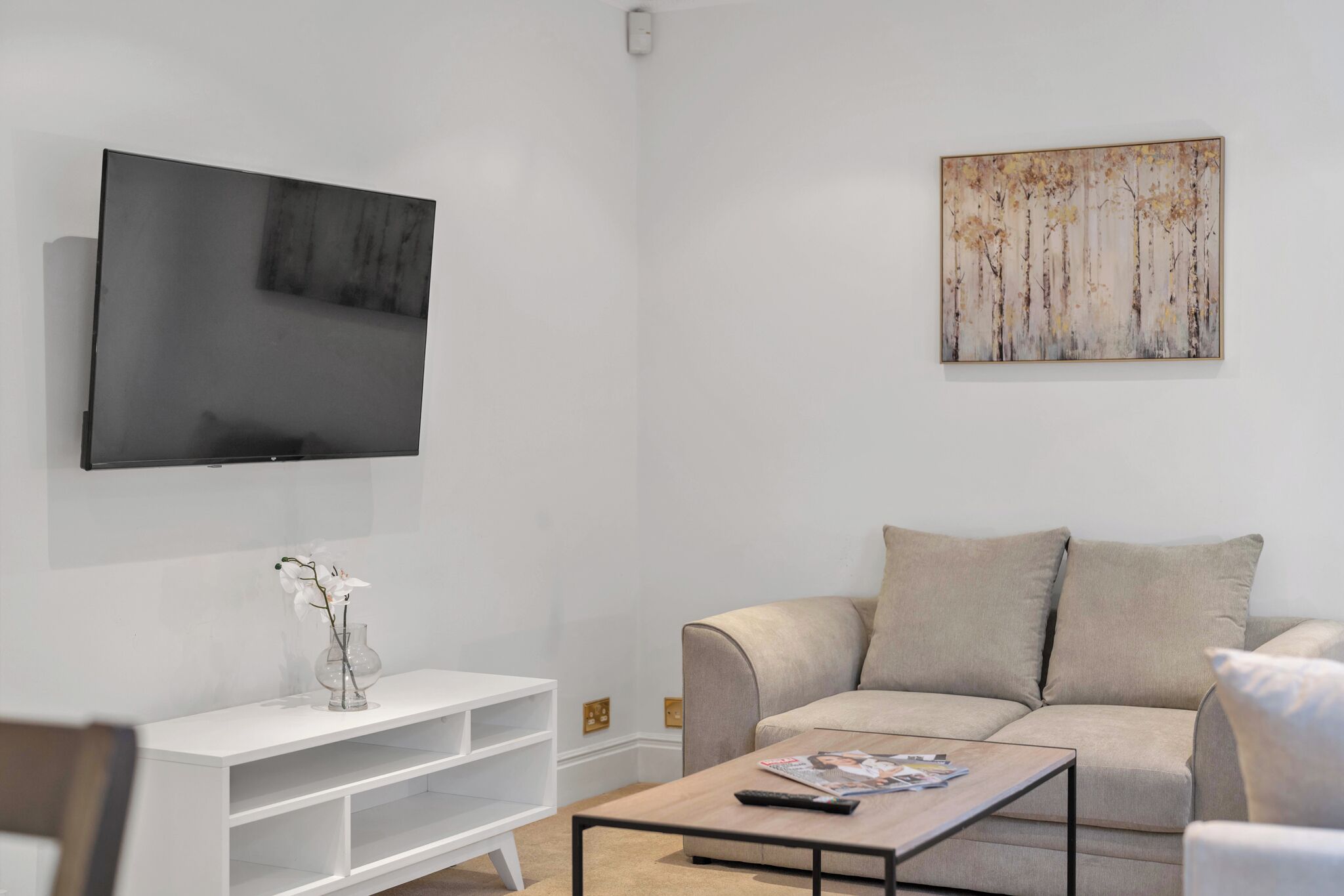 A modern living room with a flat-screen TV, a beige sofa, a coffee table, and a white entertainment unit.