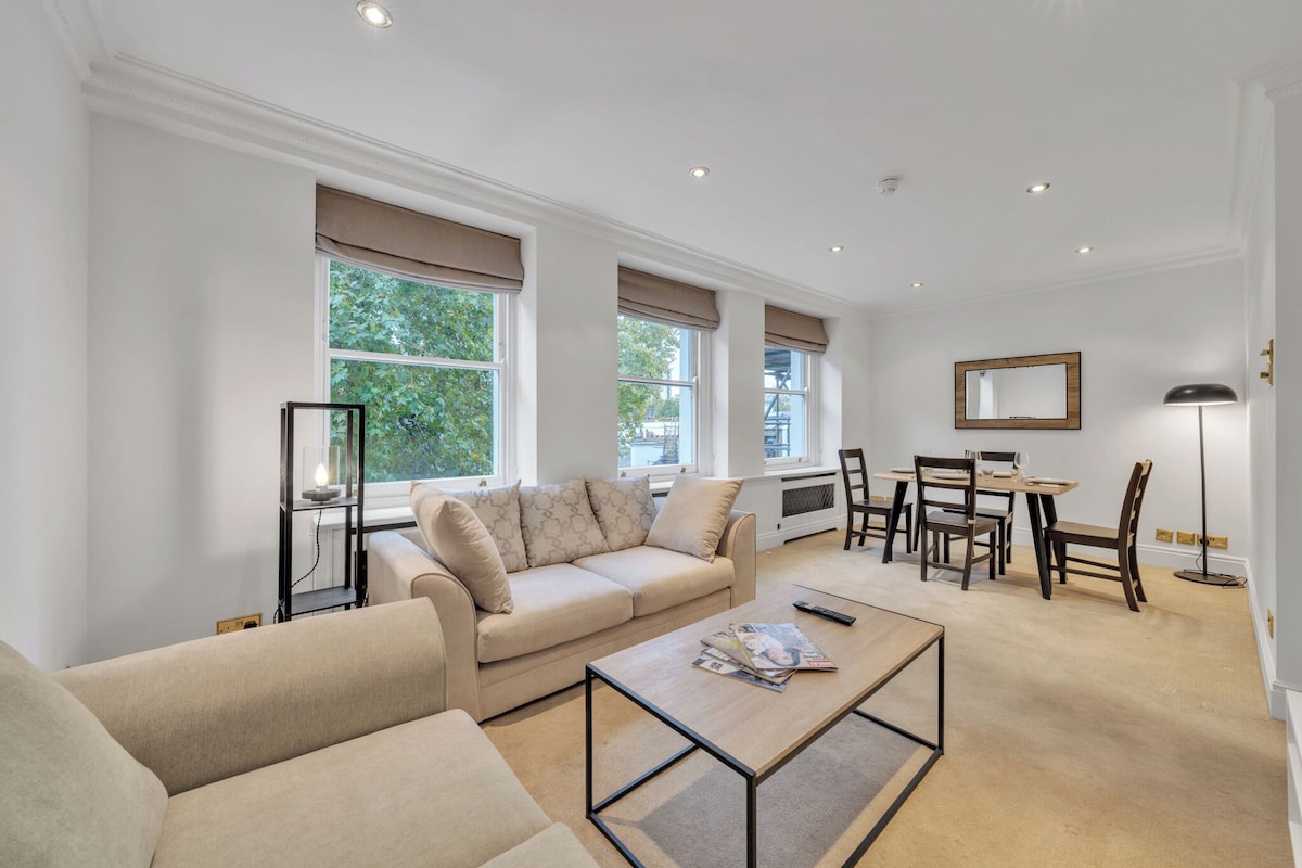 A modern living room with a beige sofa, a coffee table, and a dining area with chairs and a table.