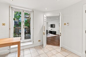 Een kamer met een houten tafel, een groot raam met uitzicht naar buiten, een flatscreen televisie aan de muur en een zwarte console.