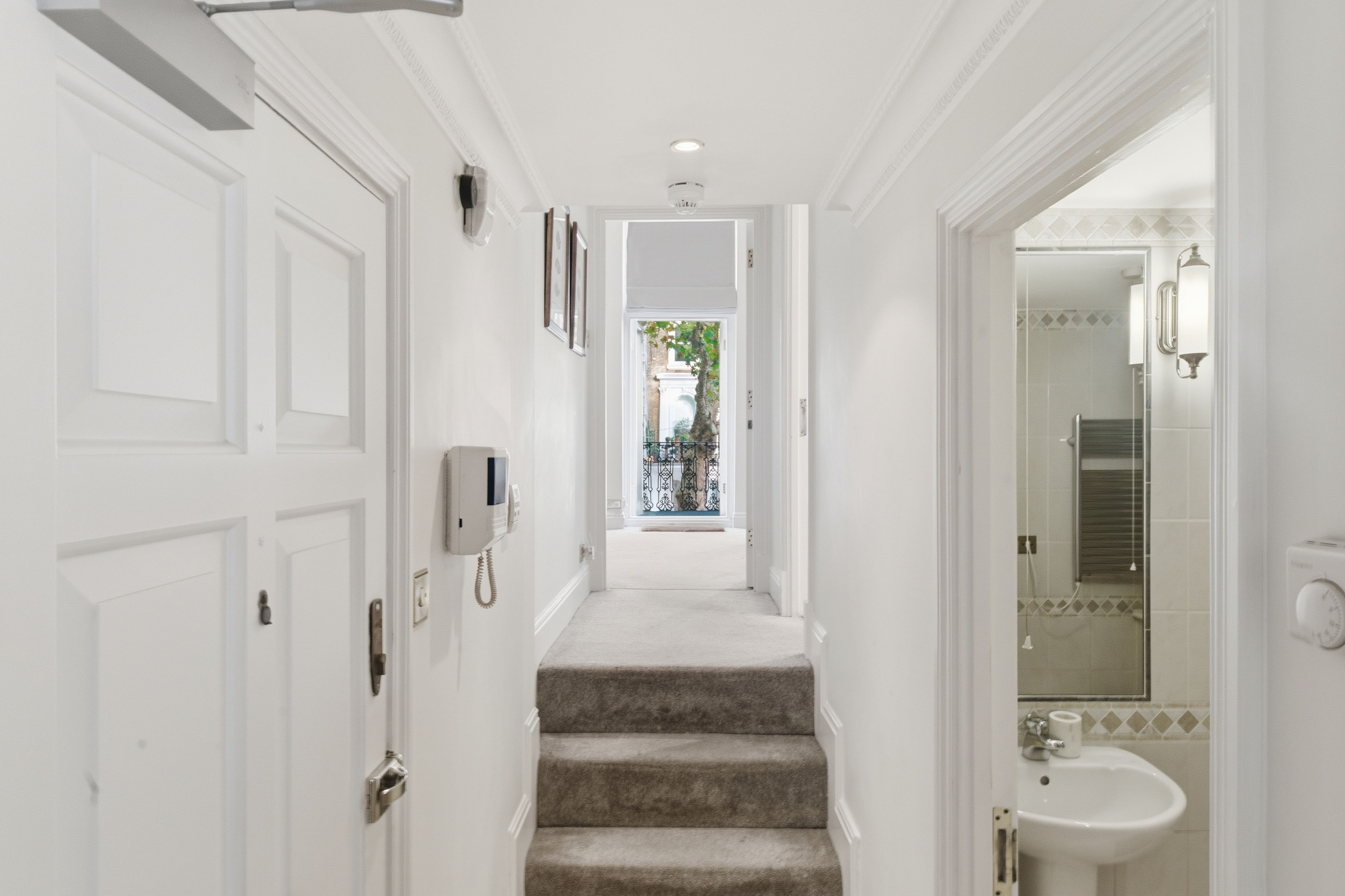 A hallway with white doors, a staircase, and a bathroom with a sink and mirror.