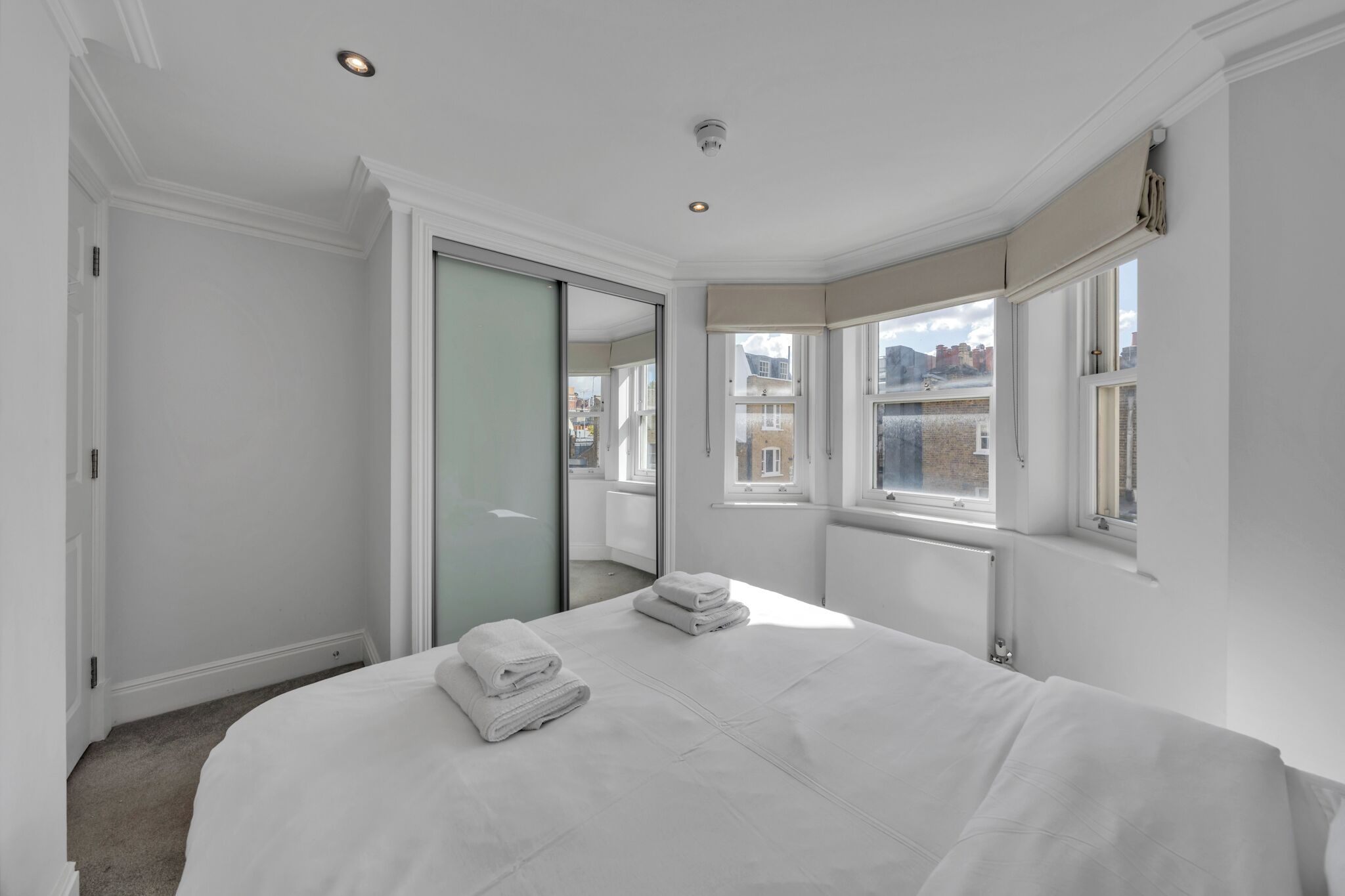 A bedroom with a large bed, a sliding glass door, and a view of the city.