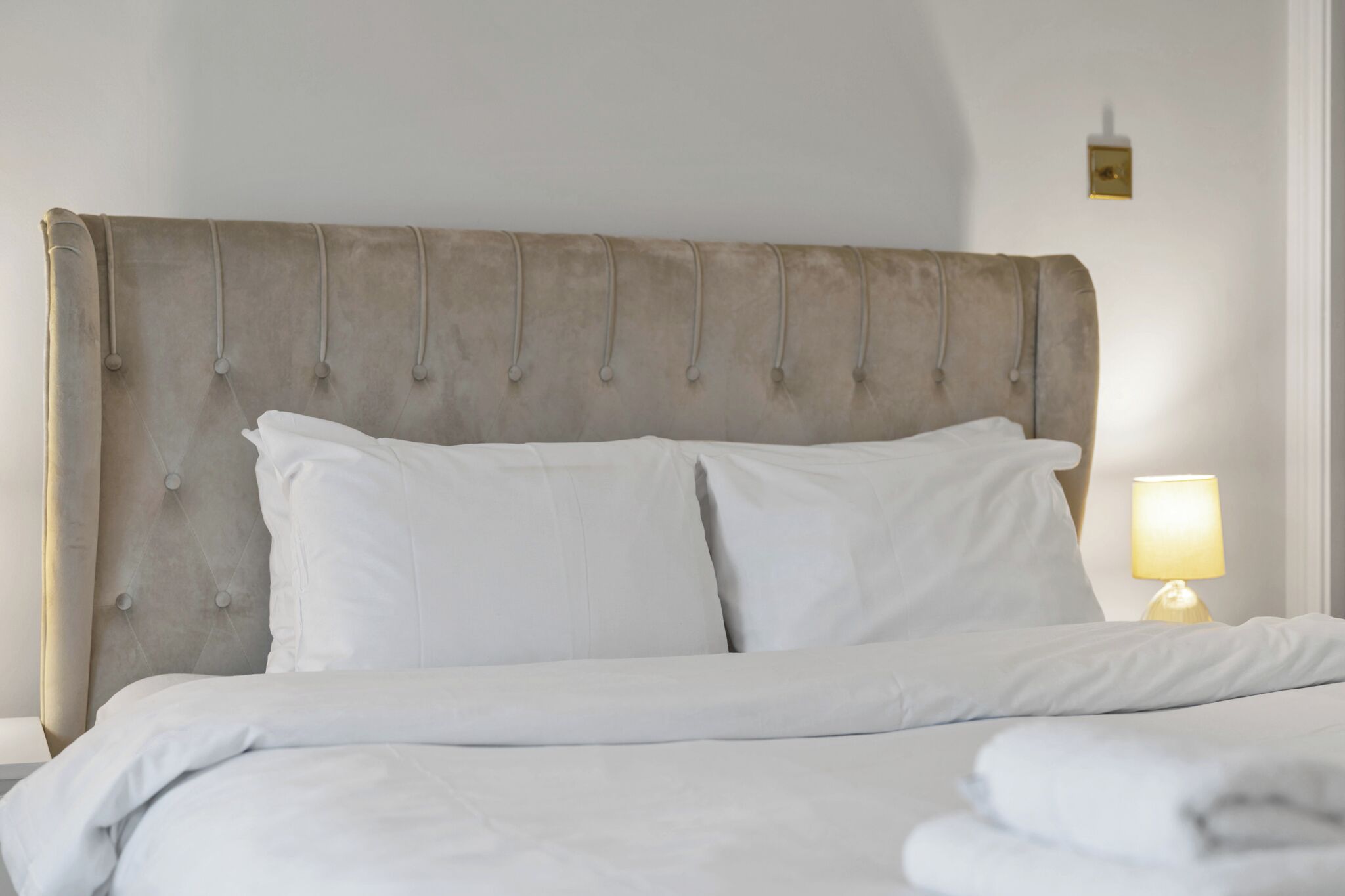 A bed with a tufted headboard, white bedding, and a bedside lamp.