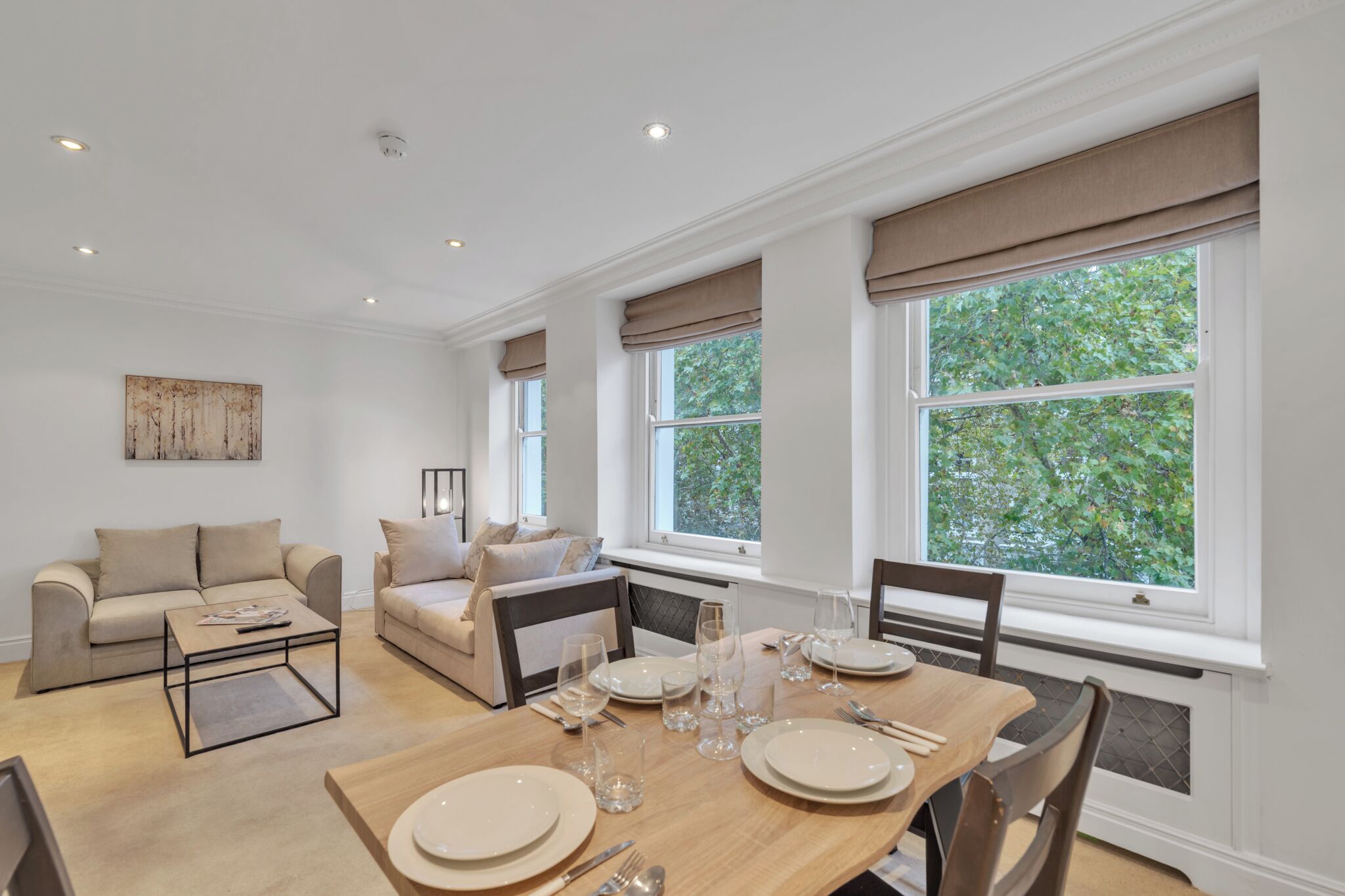 A modern living room with a dining area, large windows, and a view of greenery.