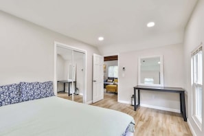 Une chambre à coucher comprenant un lit, un bureau, un miroir et une porte donnant sur une autre pièce.