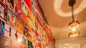 Un corridoio con una parete ricoperta di poster e quadri, che conduce a una stanza con un letto e una lampada.