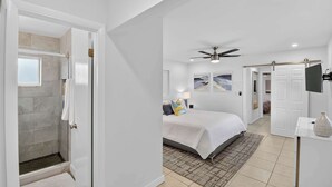 A modern bedroom with a large bed, a ceiling fan, and a shower area with a towel rack.