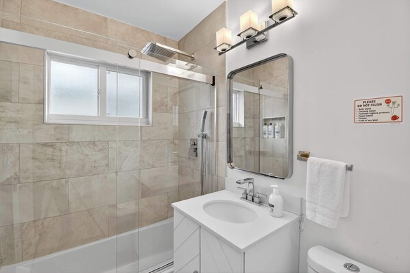 A modern bathroom with a glass-enclosed shower, a white sink, and a large mirror.