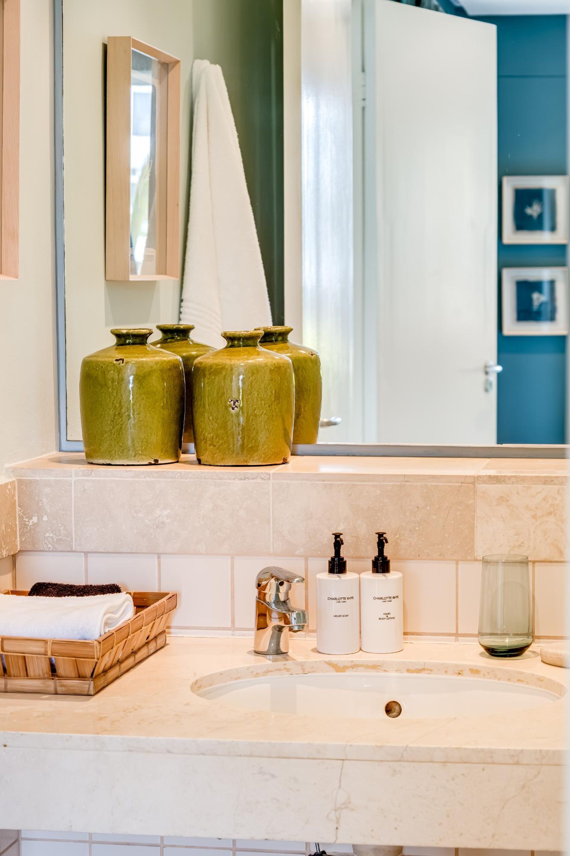 A bathroom with a marble sink, two bottles of shampoo, a glass, and a wooden basket.