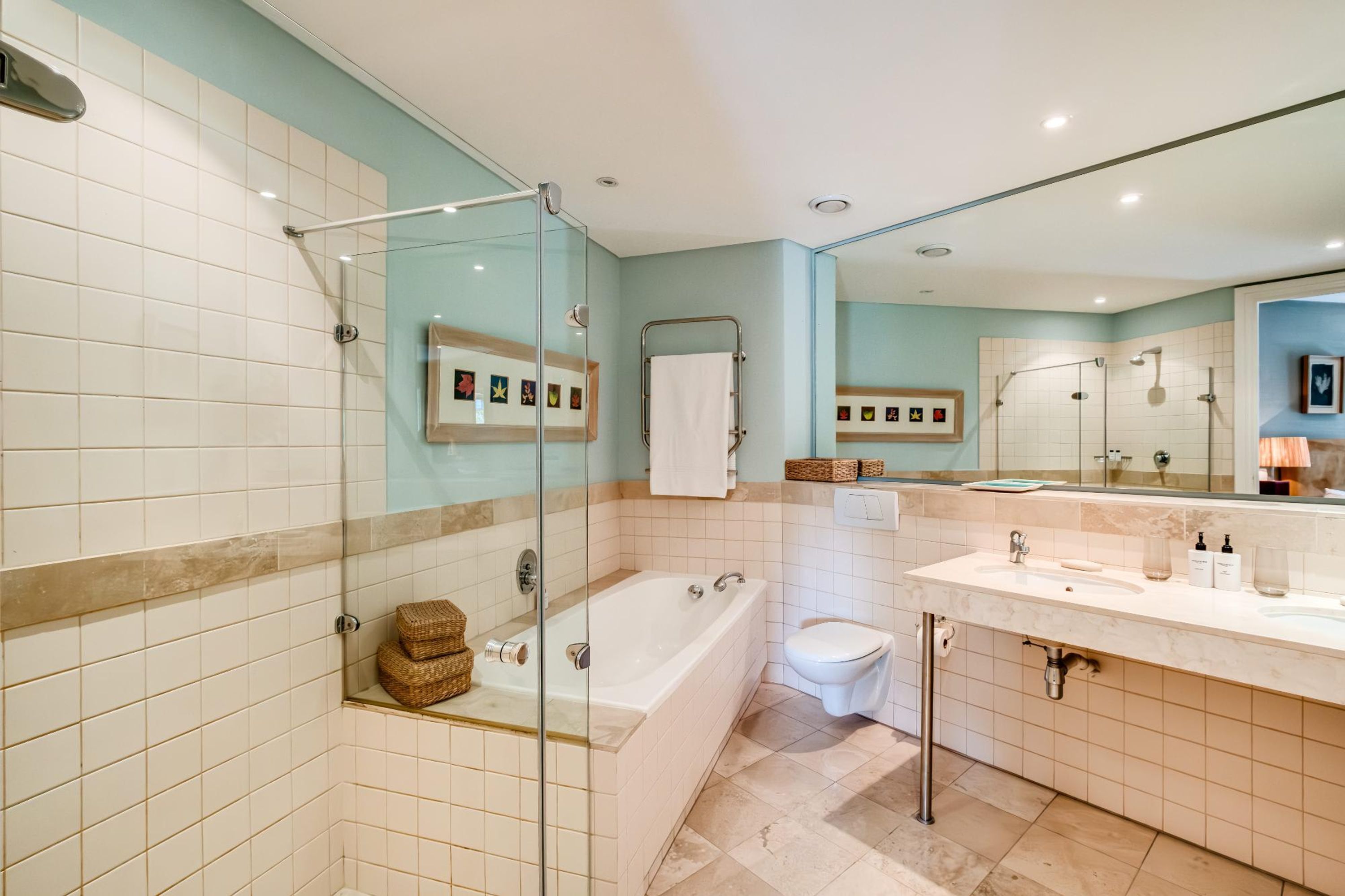 A modern bathroom with a glass-enclosed shower, a bathtub, a toilet, and a vanity with a sink and mirror.
