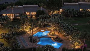 An aerial view of a resort with multiple swimming pools, lush landscaping, and well-lit buildings. - Stunning Koa Resort Condo | 2Bd/2Ba With A/C | Steps to Beach (Kihei)