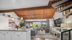 A spacious living area with a large wooden ceiling, a central island with a kitchen, a sofa set, and a TV mounted on the wall. - Stunning Koa Resort Condo | 2Bd/2Ba With A/C | Steps to Beach (Kihei)