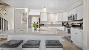 A modern kitchen with white cabinetry, stainless steel appliances, and a central island with bar stools. - Stunning Koa Resort Condo | 2Bd/2Ba With A/C | Steps to Beach (Kihei)