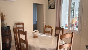 Un espace repas avec une table ronde recouverte d’une nappe blanche, entourée de chaises en bois.