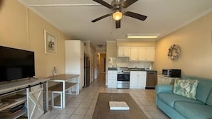 A living room with a TV, a coffee table, a sofa, and a kitchen in the background. - Resort View - Ocean Villas B115-Professionally Managed by HHB&T Vacation Rentals (Hilton Head Island)