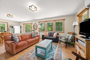 A spacious living room with a sofa, chairs, a coffee table, and a television. - Rustic and Stylish Cabin on Stunning Serene Pond (Blue Hill)