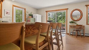 Een keuken met houten stoelen, een eettafel, een koelkast en een raam met uitzicht op groen.