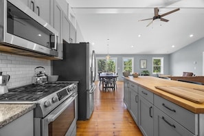 A modern kitchen with a stove, oven, and microwave, a dining area with a table and chairs, and a view of the outdoors.