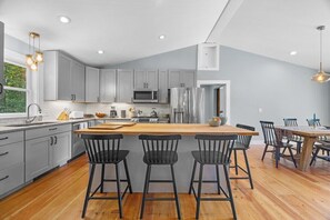 A modern kitchen with grey cabinets, a wooden island with bar stools, a stainless steel refrigerator, and a microwave. - Pondside Retreat with Private Island! (Blue Hill)