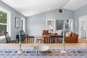 A spacious living room with a high ceiling, a dining area with a patterned rug, and a brown leather sofa. - Pondside Retreat with Private Island! (Blue Hill)