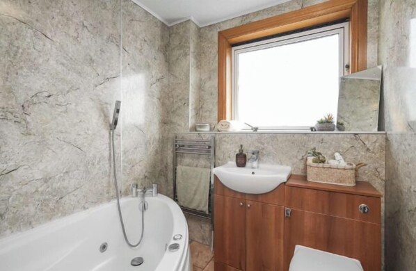 Een badkamer met een marmeren wand, een houten wastafelmeubel, een wastafel en een bad.