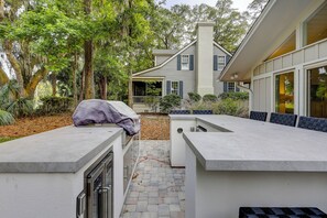 A modern house with a covered outdoor seating area, a stone pathway, and a large window overlooking the yard. - 259 Greenwood Drive - Escape to Coastal Elegance (Hilton Head Island)