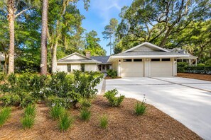 A two-story house with a garage, surrounded by trees and landscaped with shrubs and mulch. - 259 Greenwood Drive - Escape to Coastal Elegance (Hilton Head Island)
