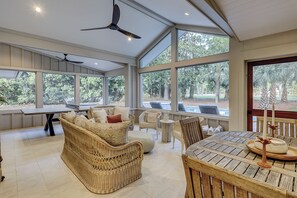 A spacious room with large windows, a ceiling fan, wicker furniture, and a dining table. - 259 Greenwood Drive - Escape to Coastal Elegance (Hilton Head Island)