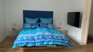 A bed with a patterned blue and white duvet, two bedside tables with lamps, and a flat-screen TV on the wall.