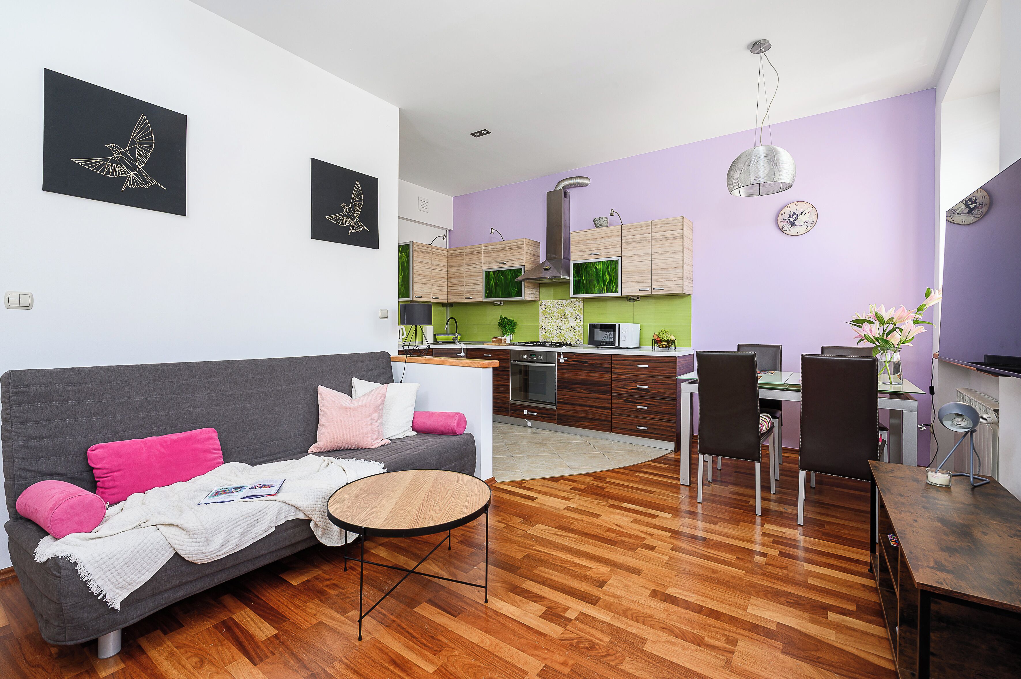 Eine moderne Wohnung mit grauem Sofa, einem Esstisch und einer Küchenzeile mit Holzschränken und einem Herd.