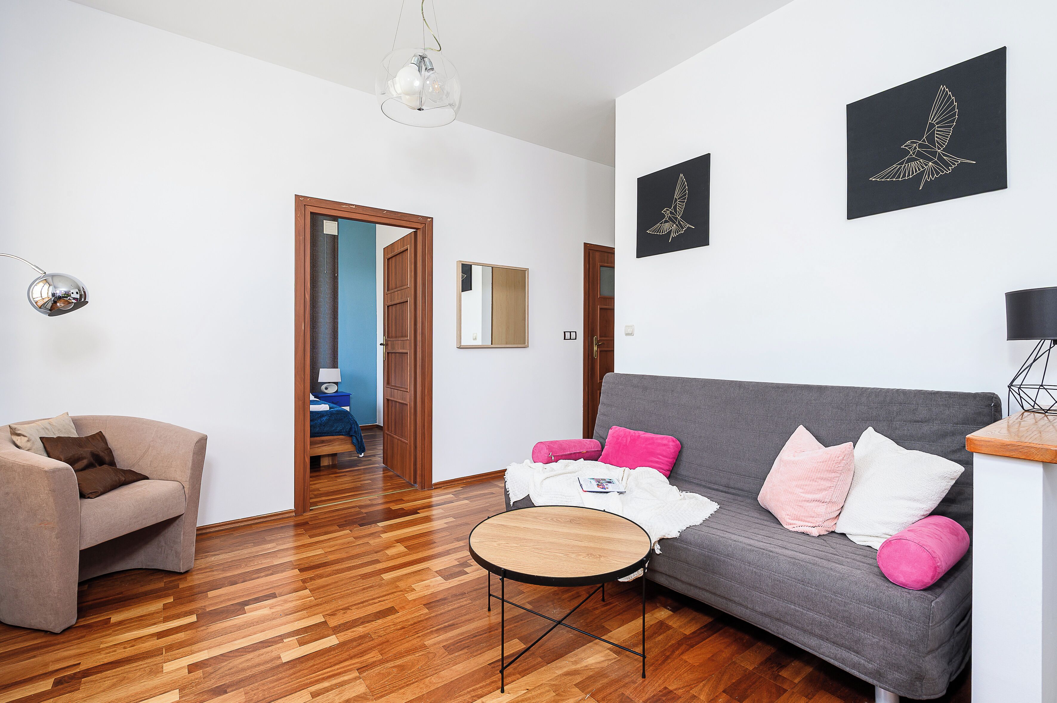Una sala de estar moderna con un sofá gris, una mesa de centro redonda de madera y un sillón beige.