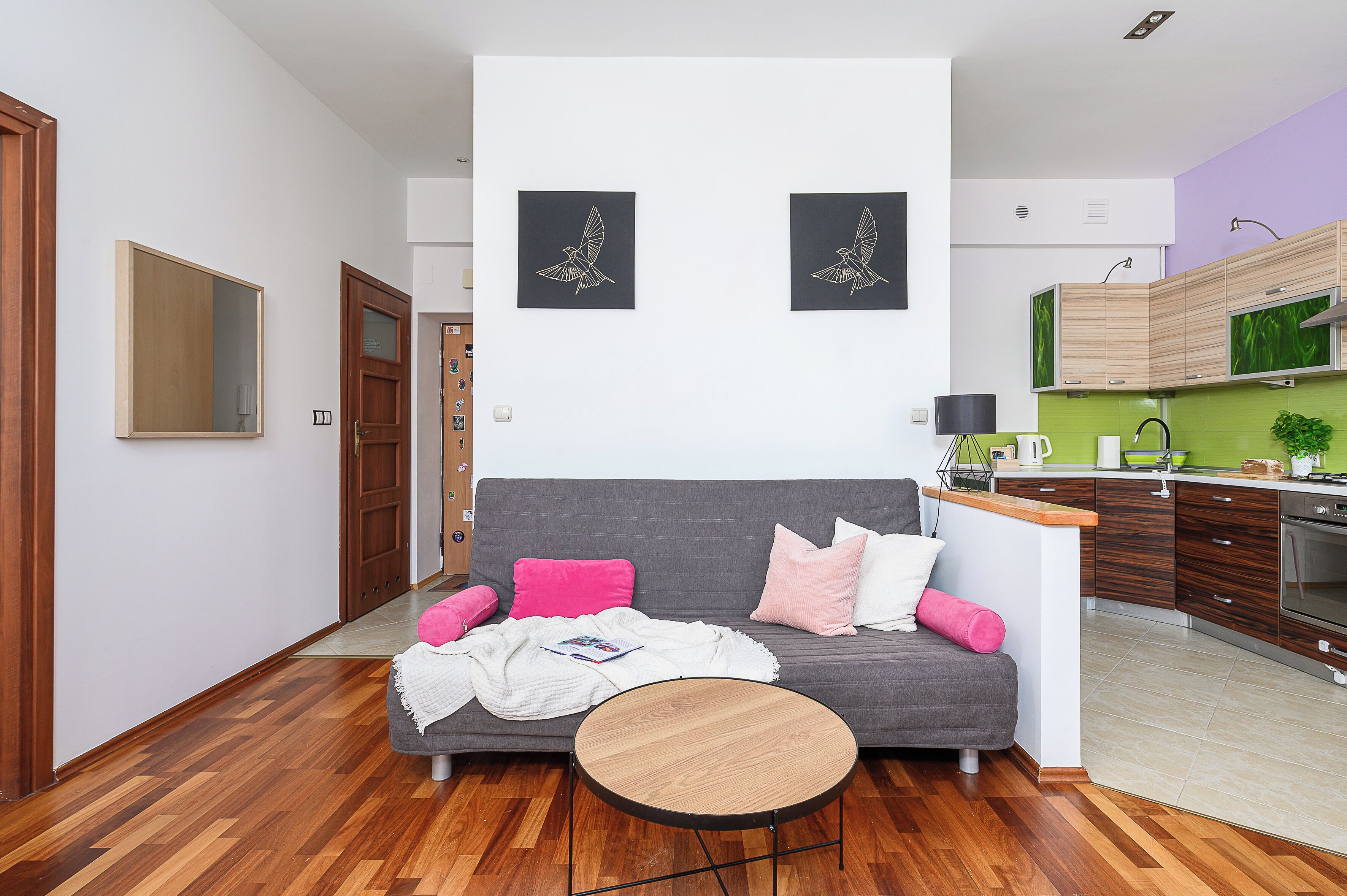 A modern living room with a grey sofa, a round wooden coffee table, and two black framed wall art pieces.