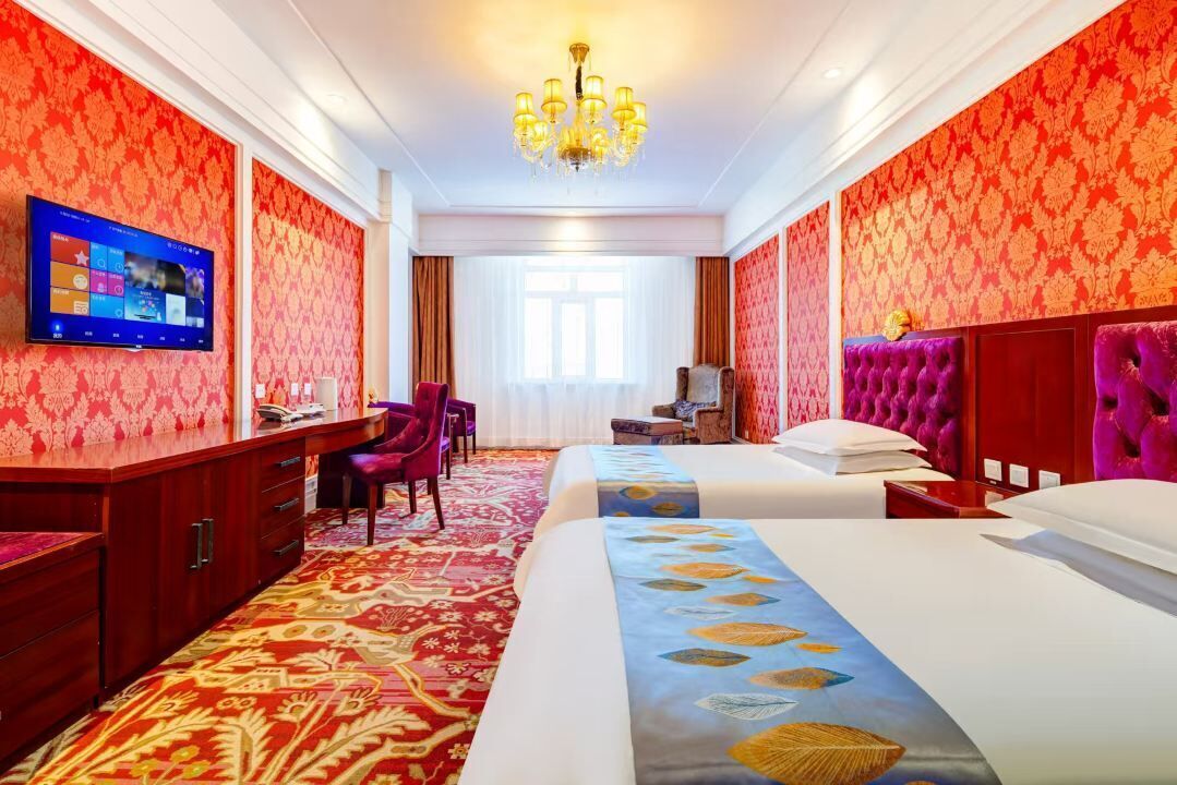 A hotel room with two beds, a TV on the wall, a desk, and a chair.