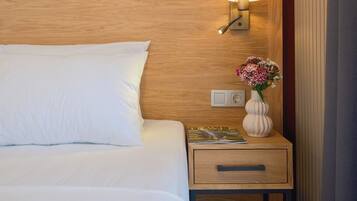 A hotel room with a wooden headboard, a bedside lamp, a nightstand with a vase of flowers, and a drawer.