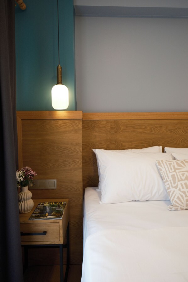 A neatly made bed with white bedding and a wooden headboard, a bedside table with a lamp, and a magazine on the table.
