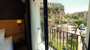 A hotel room with a balcony overlooking a street with cars and buildings.