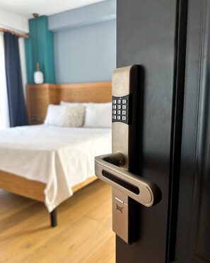 A modern hotel room with a bed, a door with a numeric keypad lock, and a wooden headboard.