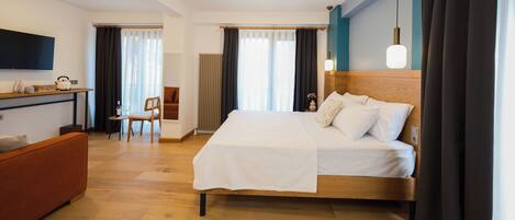 A hotel room with a wooden bed, a desk with a chair, a sofa, and a TV on the wall.