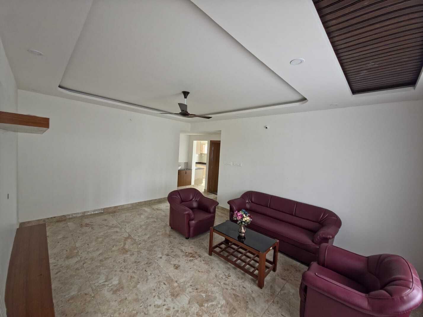 Un salon spacieux avec un plafond haut, un ventilateur de plafond, un canapé, deux fauteuils et une table basse.