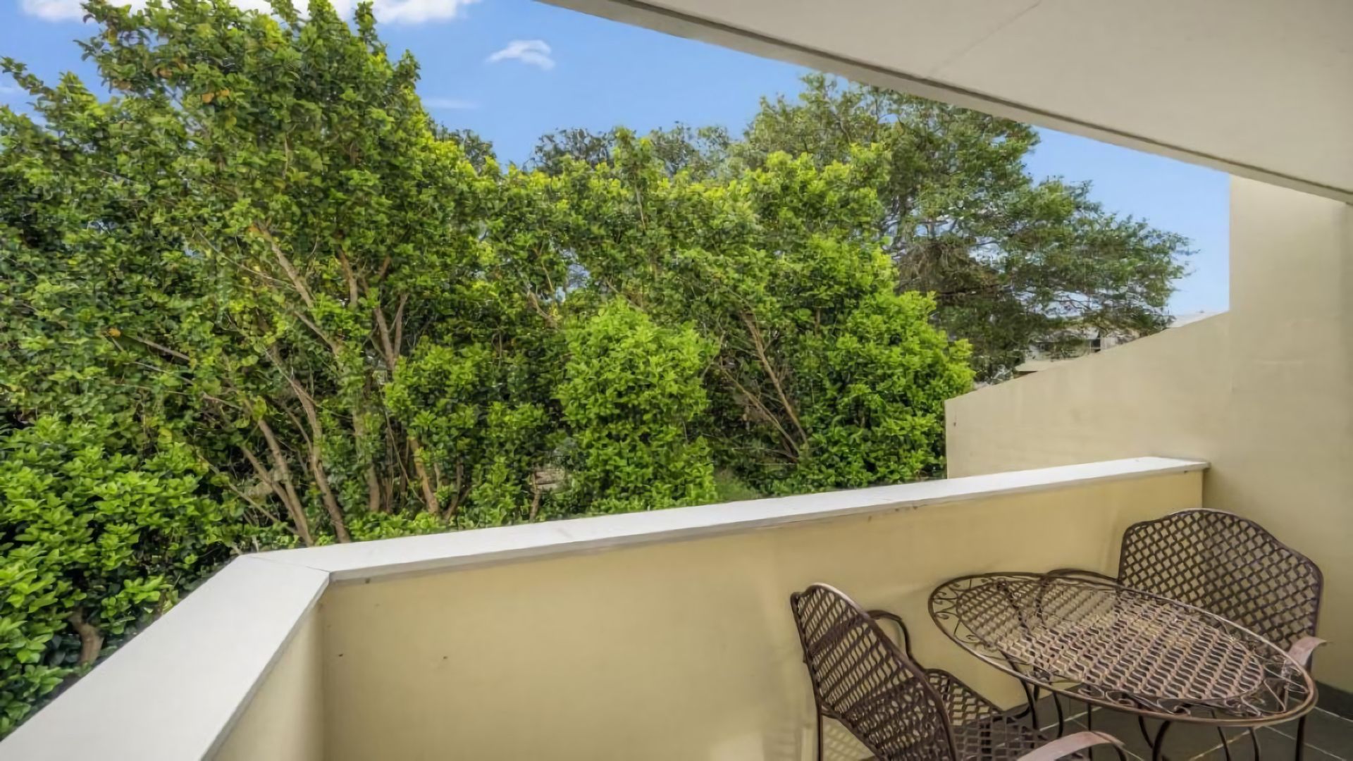 A balcony with a table and chairs, surrounded by dense green foliage.