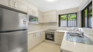 Una cocina moderna con electrodomésticos de acero inoxidable, armarios blancos y un ventanal que proporciona luz natural.