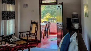 A hotel room with a bed, a dining table with chairs, a window with curtains, a sign prohibiting smoking, and a view of greenery outside. - Willow Cottage Ella (Ella)