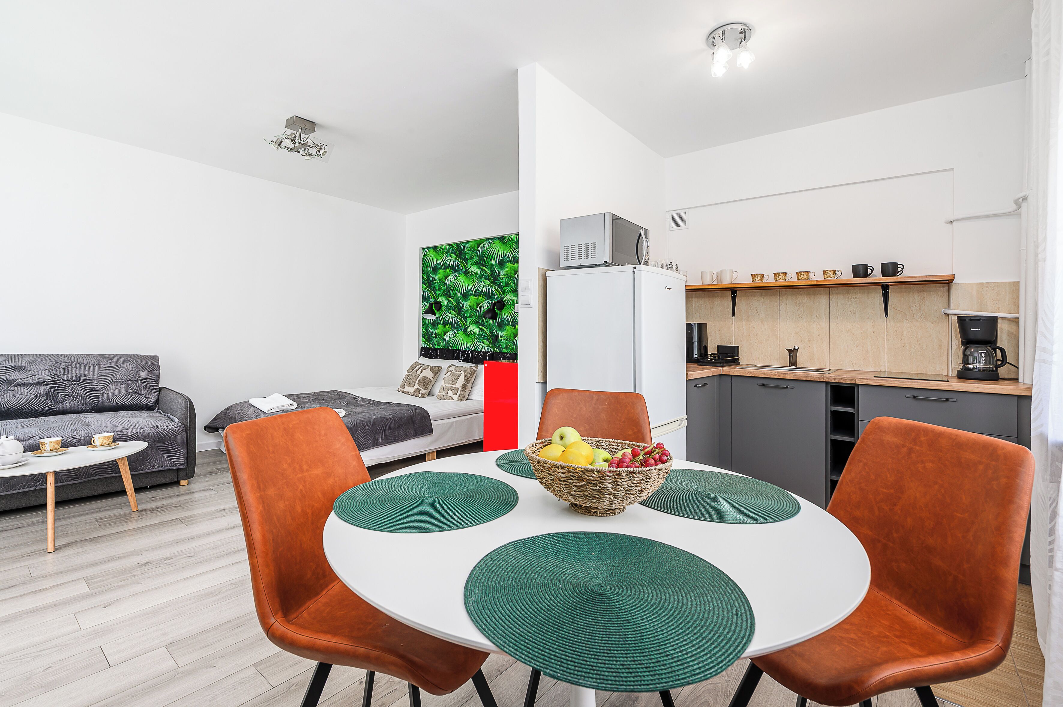 Un salon moderne avec un canapé gris, une petite table blanche et un coin repas comprenant une table blanche et des chaises orange.