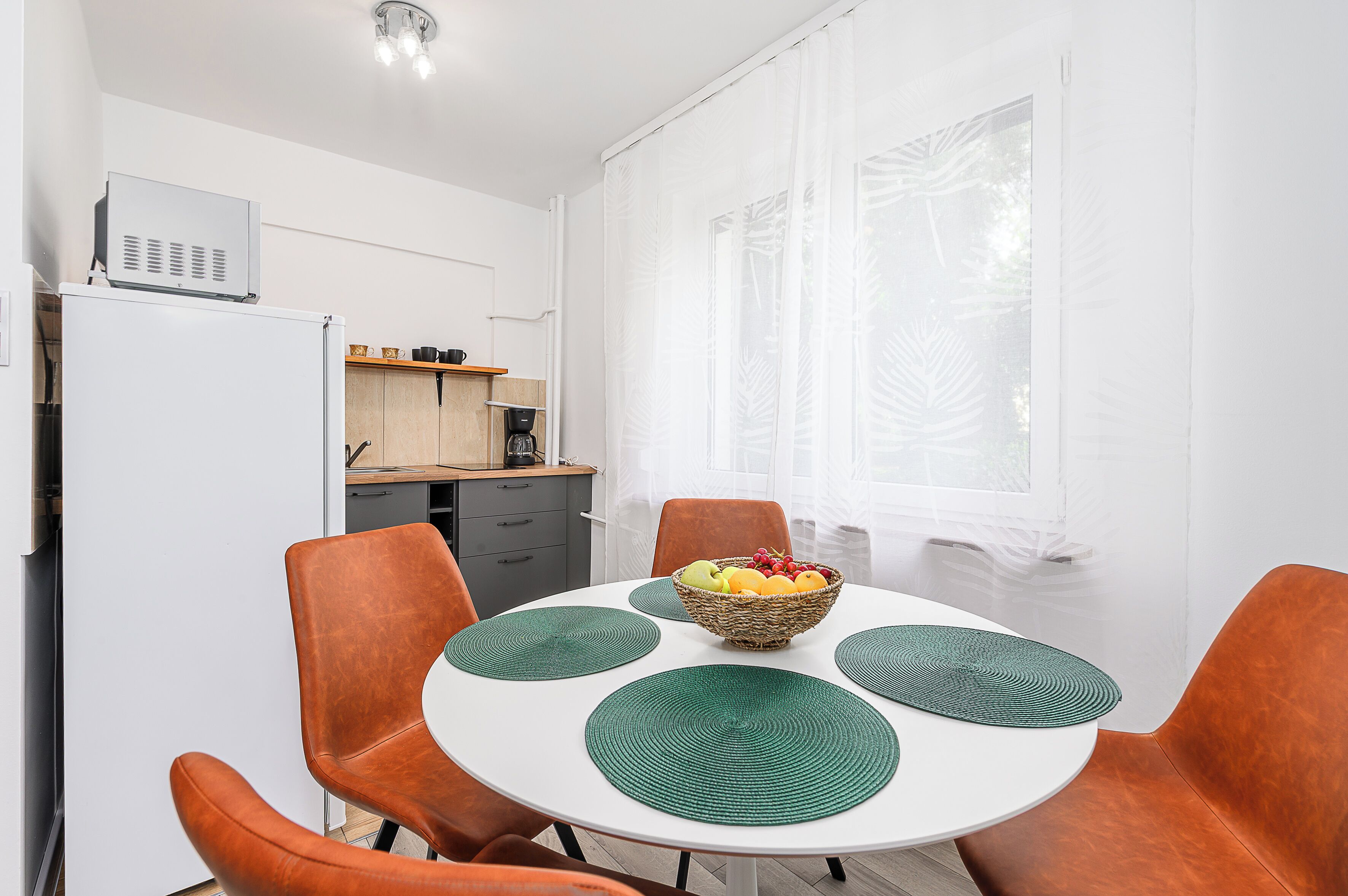 Un coin repas avec une table ronde, des chaises orange et un saladier rempli de fruits.