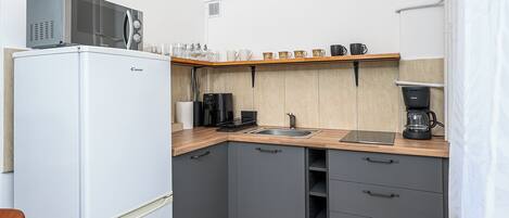 A compact kitchen with a refrigerator, microwave, coffee maker, and a shelf with cups and glasses.