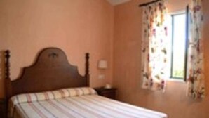 Un dormitorio con una cama individual, una mesita de noche, una ventana con cortinas florales y una pared lisa.