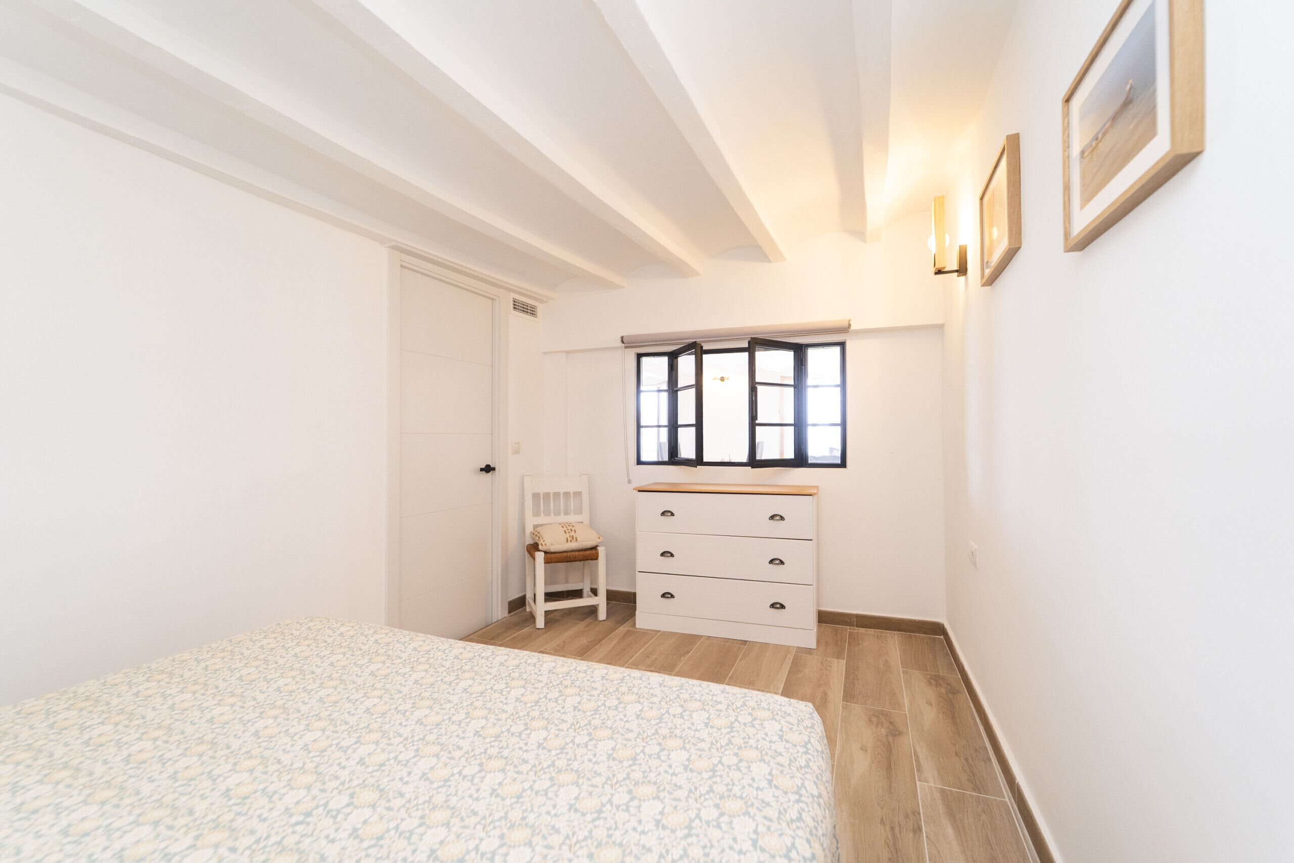 A bedroom with a bed, a chair, a dresser, and a window with blinds.