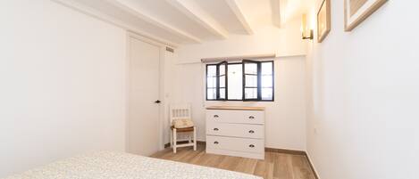 A bedroom with a bed, a chair, a dresser, and a window with blinds.
